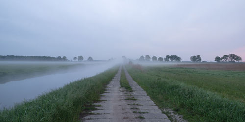 Dirt road amidst field against sky