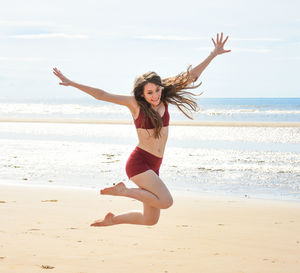 Young woman with arms raised on beach against sky