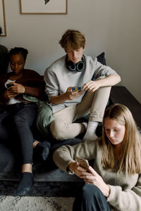 Teenage girls and boy using mobile phone while sitting in living room