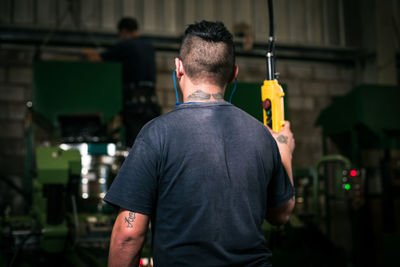 Rear view of worker operating machinery at factory