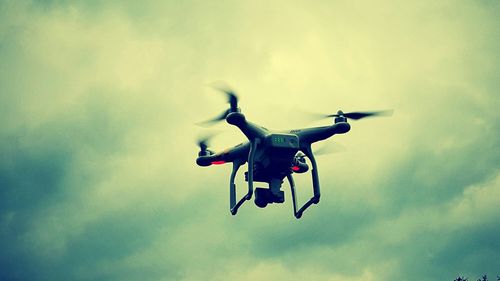 Low angle view of quadcopter flying against cloudy sky