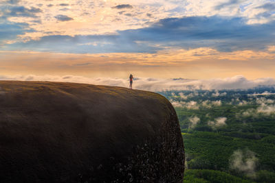 Mid distance of woman standing on mountain against cloudy sky during sunset