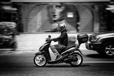 Side view of man riding motor scooter on street