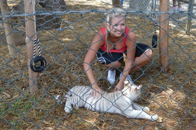 Smiling young woman stroking white tiger cub at zoo