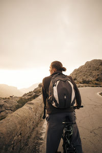 Young male backpacker with bicycle looking at mountains against sky