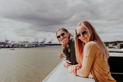Portrait of young women standing at dock against cloudy sky