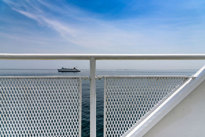 Ship in sea against sky seen from white metallic railing