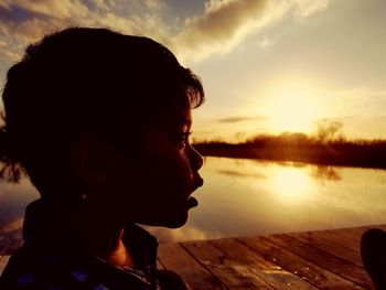 Side view of silhouette boy looking away while standing on pier over lake during sunset