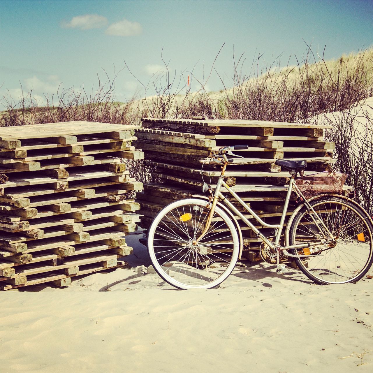 transportation, bicycle, mode of transport, beach, stationary, sky, land vehicle, sand, wheel, parked, day, sunlight, abandoned, outdoors, stack, large group of objects, no people, parking, nature, absence