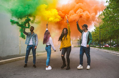 Full length of friends holding distress flare standing on road