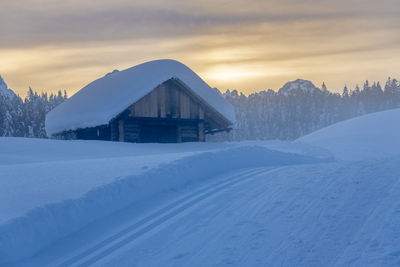 Snow covered landscape against sky during sunset