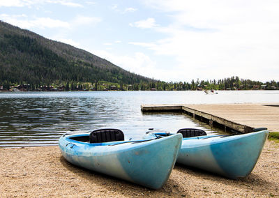 Boats moored at lakeshore against cloudy sky