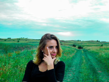 Close-up of beautiful young woman on grassy field against cloudy sky