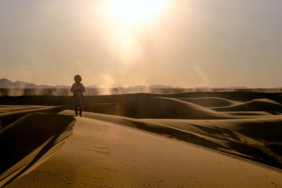 Man standing in sand dunes against bright sky