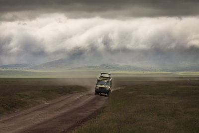 Car on road amidst field against sky