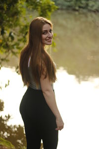 High angle portrait of smiling woman standing at lakeshore in park