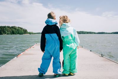 Siblings stood holding hands looking at the sea at the beach together