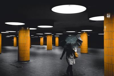 Woman walking under umbrella at illuminated garage