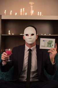 Man wearing mask while holding drink and currency in frame at hotel