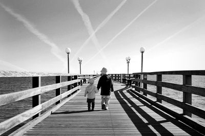 Rear view of man walking on jetty against sea