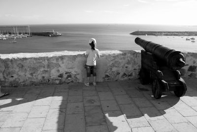 Rear view of girl standing by cannon at observation point against sea