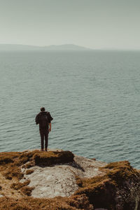 Rear view of man standing on cliff against sea