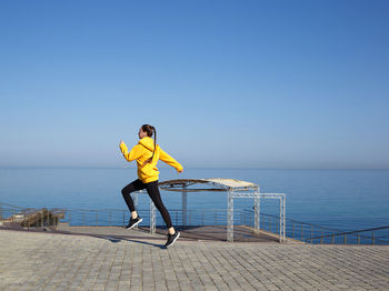 Man with umbrella against sea against clear sky