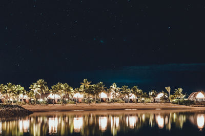 Reflection of illuminated trees in lake against sky at night