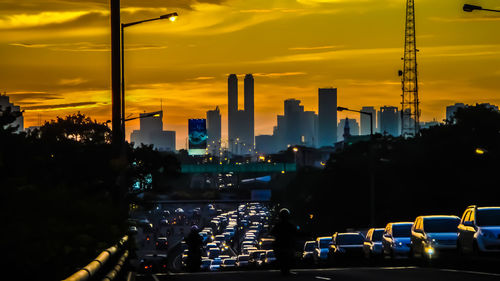 Cars on road against buildings during sunset