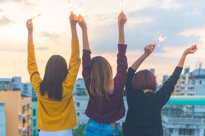 Rear view of female friends with sparklers against sky in city