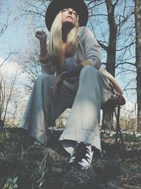 Young woman looking away while sitting on tree in forest