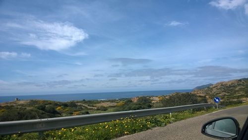 View of road by sea against cloudy sky