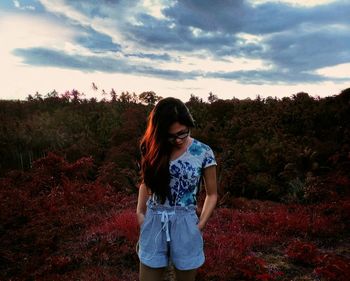 Young woman standing on field against sky