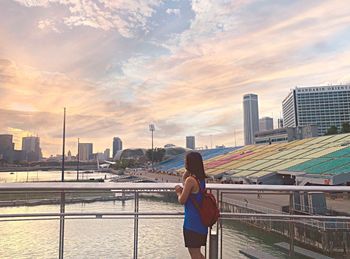 Woman on railing against buildings in city during sunset