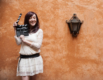 Portrait of beautiful woman holding film slate against orange wall