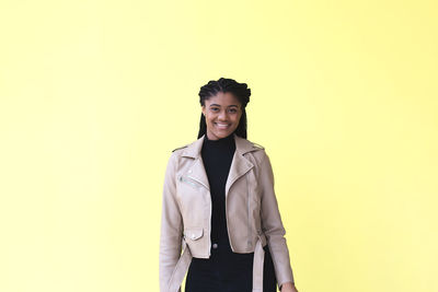 Portrait of smiling young woman against yellow background