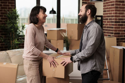 Happy man and woman with box standing at home