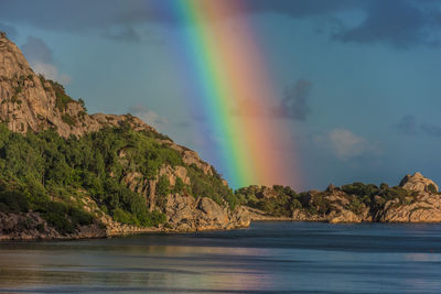 Scenic view of rainbow over sea and mountains