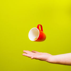Close-up of hand holding balloon against yellow background