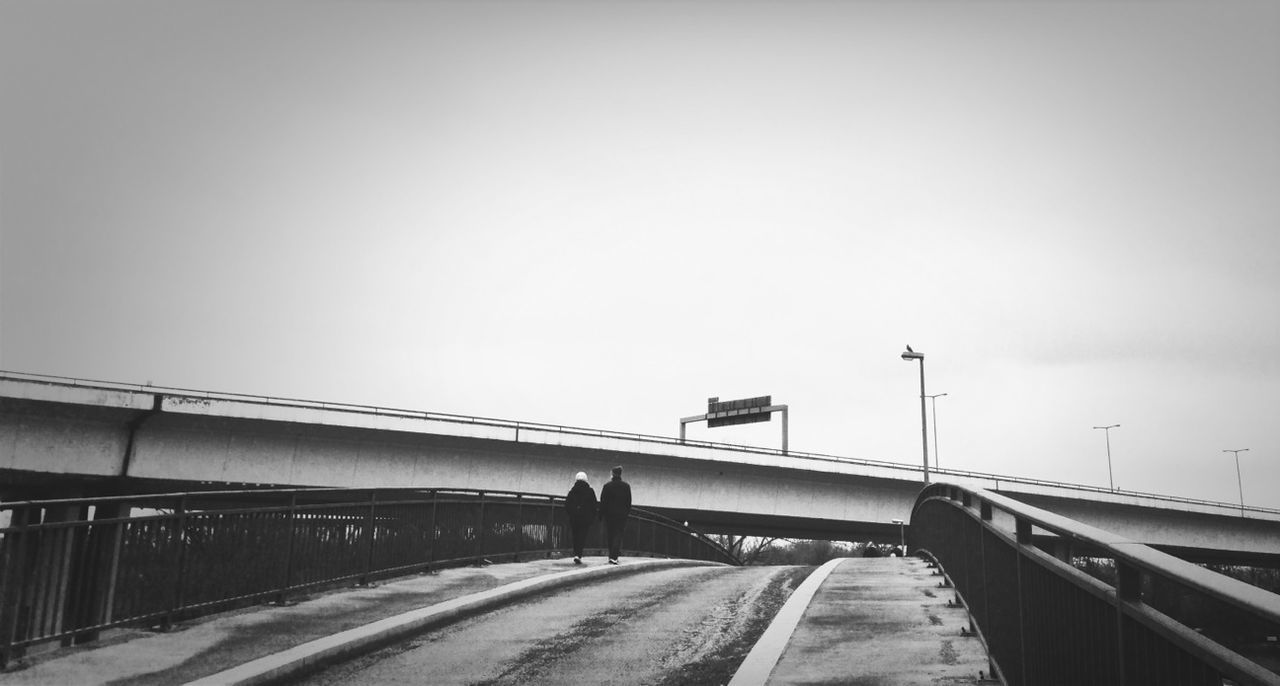 transportation, the way forward, railing, clear sky, men, lifestyles, walking, built structure, copy space, architecture, bridge - man made structure, connection, full length, rear view, diminishing perspective, leisure activity, sky, person