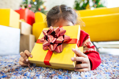 Close-up of girl holding christmas present while lying on rug