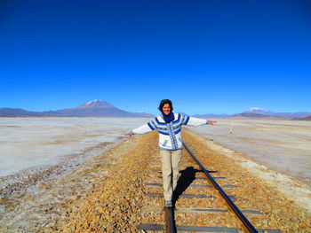 Happy woman walking with arms outstretched on railroad track at salar de uyuni