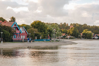 Trees and houses by river against sky