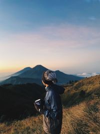 Rear view of man standing on mountain against sky during sunset