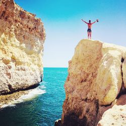 Man standing on cliff by sea against clear sky