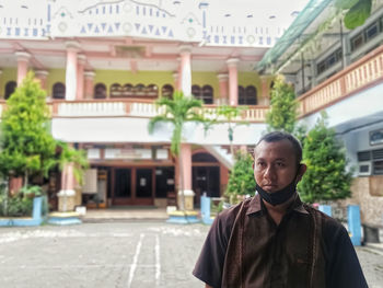Portrait of young man standing against buildings in city
