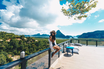 Portrait of woman sitting on railing against sky