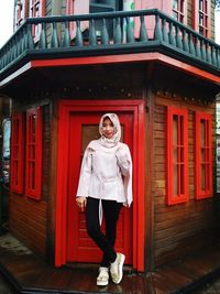 Portrait of young woman standing against building