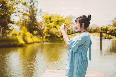 Woman standing by lake against trees