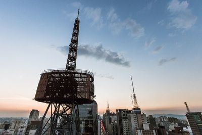 Low angle view of crane and buildings against sky during sunset